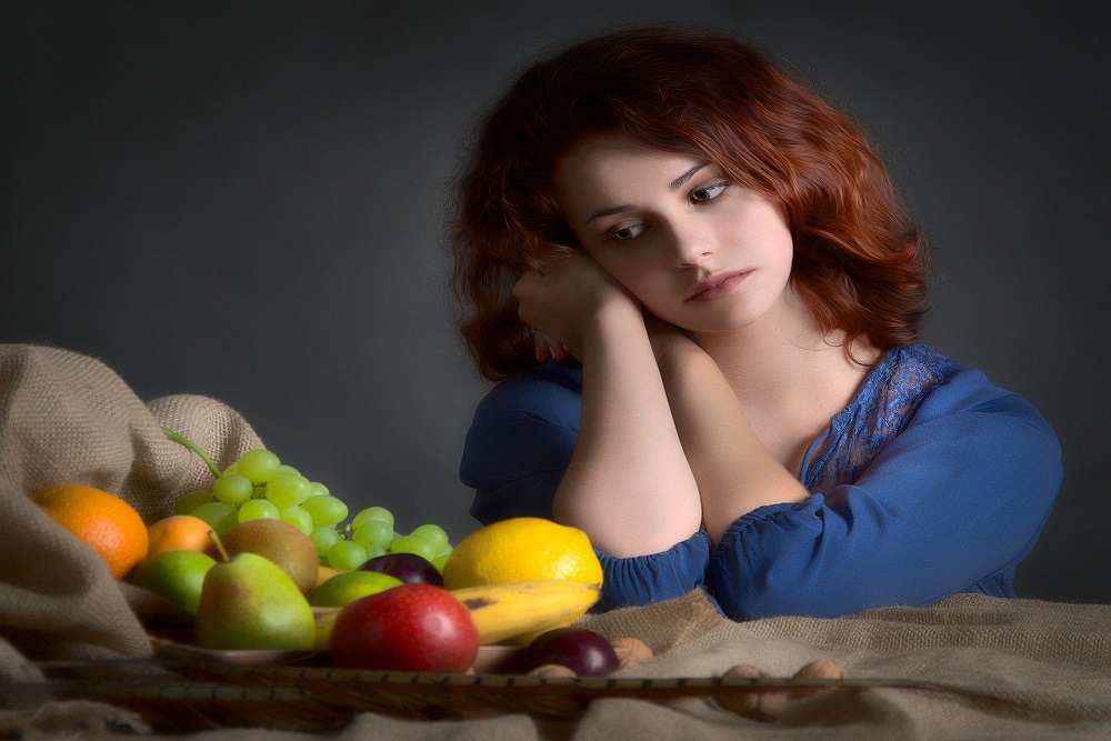 žena smutně kouká na ovoce na stole