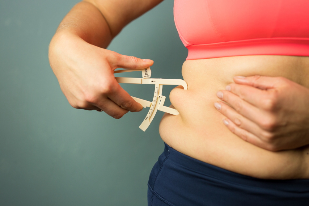 Žena si měří tělesný tuk v oblasti břicha 