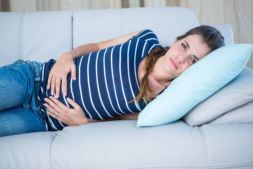 Žena leží na pohovce s bolestí břicha