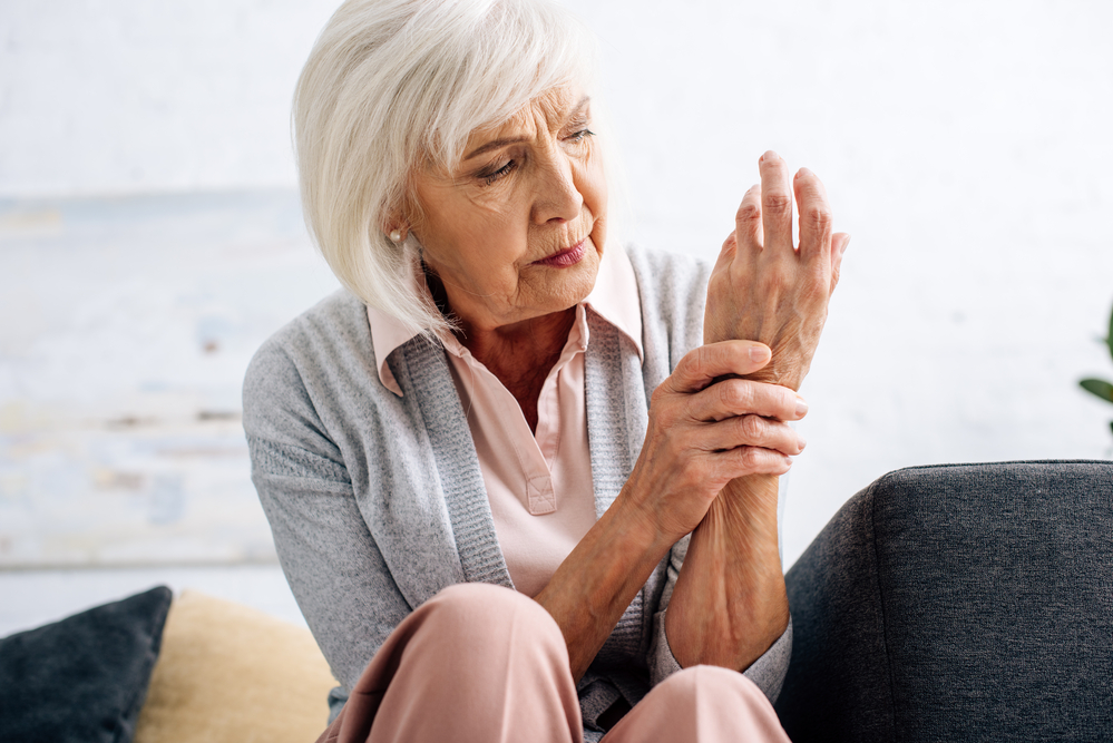 Žena pozoruje své ruce postižené revmatoidní artritidou