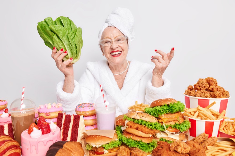 zdravé a nezdravé jídlo, starší žena u stolu plného hamburgerů a zákusků