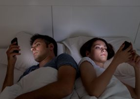 Mladý pár s mobilem v posteli