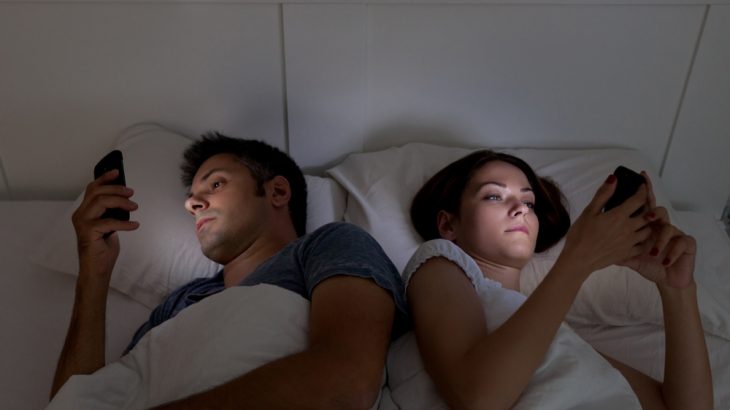Mladý pár s mobilem v posteli