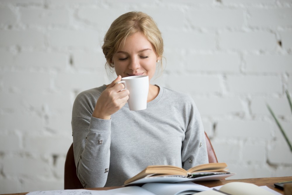 Mladá žena inhalující výpary z čaje nad knihou