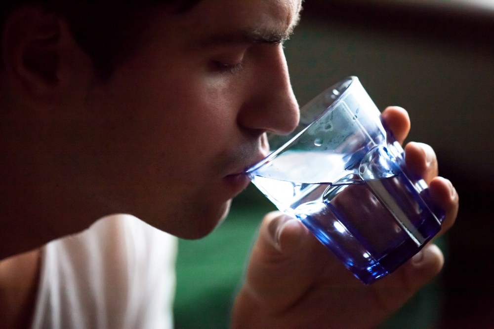 Mladý muž pijící ze sklenice vody s jablečným octem