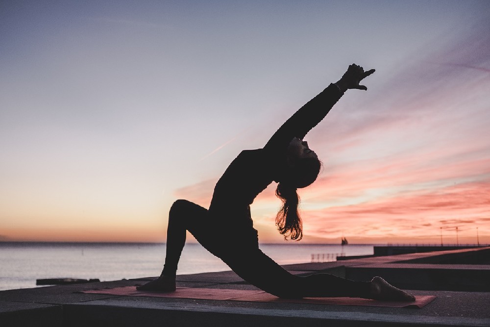 Mladá žena cvičící jógu venku v přírodě při západu slunce