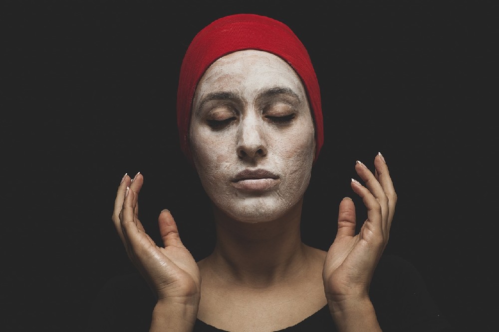 Žena v červené čepici s nanesenou přírodní pleťovou maskou