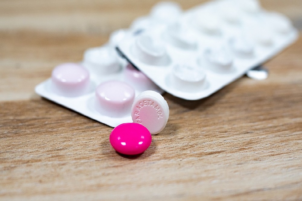 Růžová a bílá tableta paracetamolu a ibuprofenu s platíčky v pozadí
