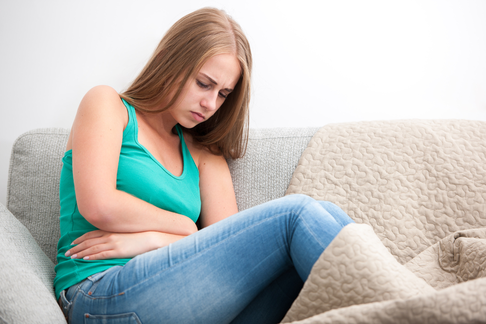 Žena sedí na pohovce s bolestí břicha 