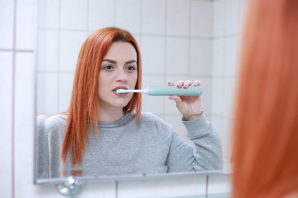 Mladá žena s měděnými vlasy si čistí zuby před zrcadlem