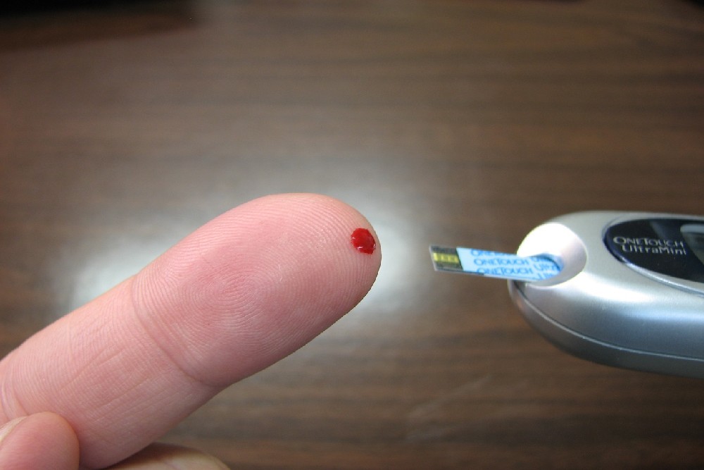 Detail kapky krve na špičce prstu s domácím glukometrem připraveným k měření hladiny krevního cukru