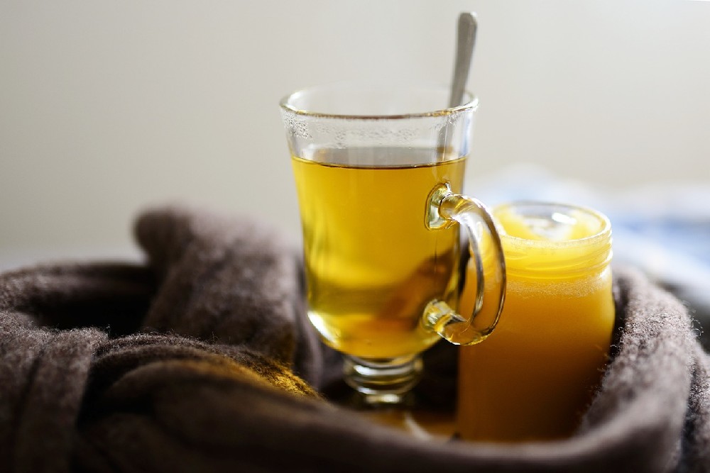 Čaj ve sklenici s ouškem, vedle něj stojí sklenička medu. Obě nádoby jsou zabalené šálou
