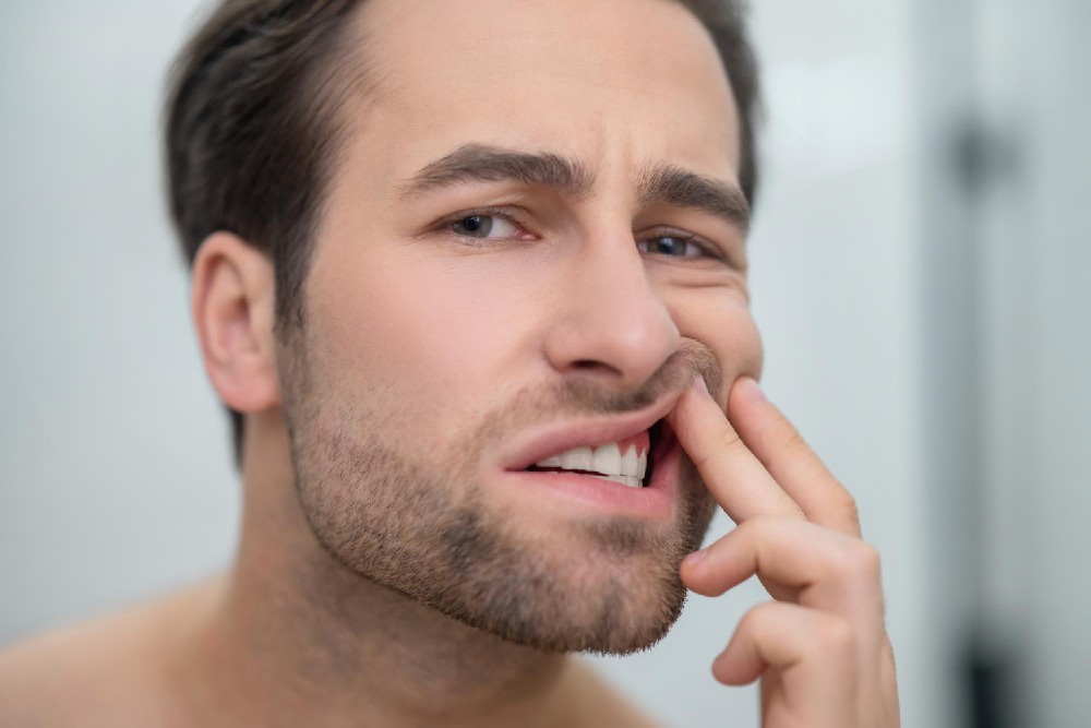 Mladý muž, který s obavami sleduje stav dásní a prstem si pozdvihuje koutek rtu