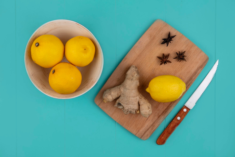 Citrony v misce, vedle nich na prkénku zázvor, citron, koření a nůž