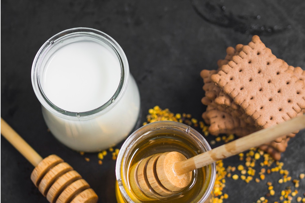 Pohled shora na sklenici mléka a medu se sušenkami