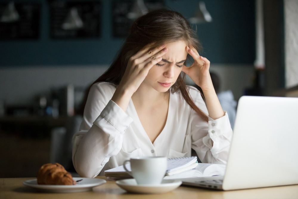 Mladá žena s bolestí hlavy držící se za čelo při práci na notebooku
