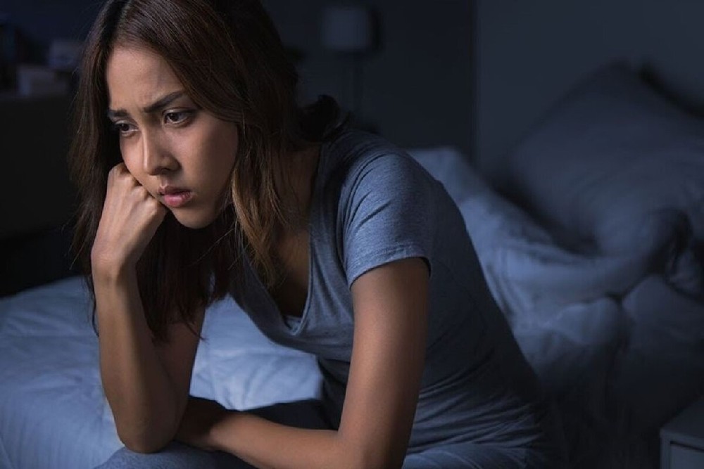 Žena sedící po tmě na posteli, unavená a skleslá