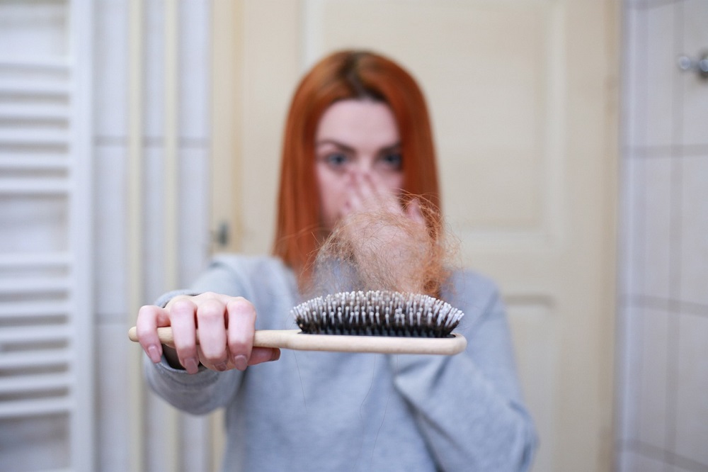 Žena drží kartáč na vlasy plný vypadaných vlasů - na vině může být stres.
