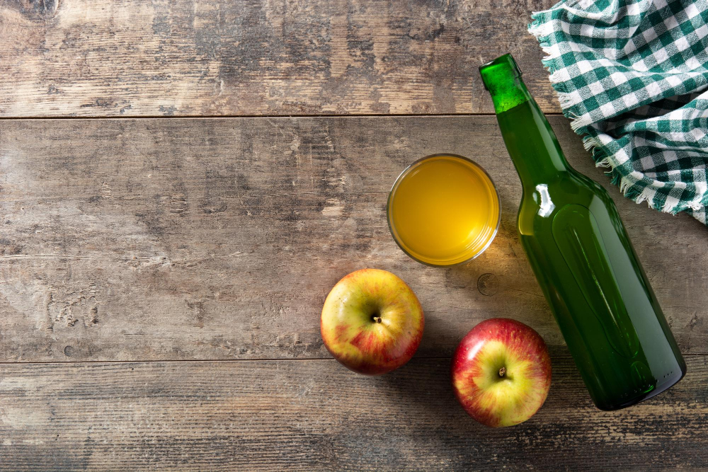 Láhev jablečného octa, sklenička a dvě jablka položená na stole