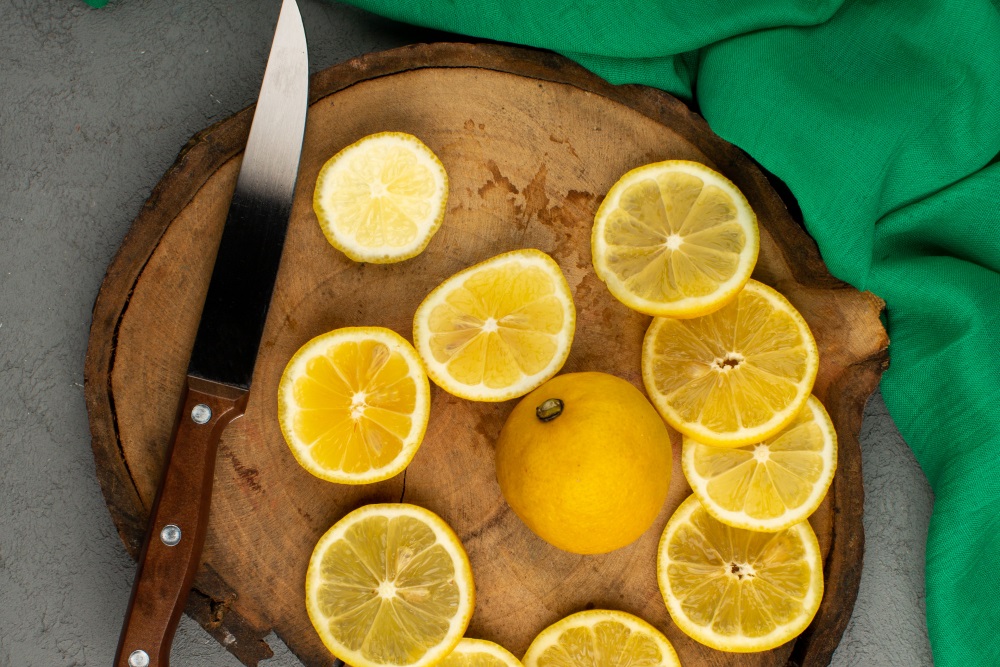 Plátky citronu s nožem nakrájené na dřevěném kulatém prkénku položeném na posteli