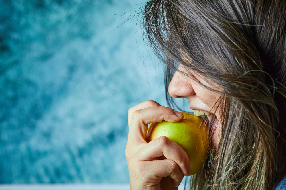 Žena z profilu jak jí jablko na modrém pozadí