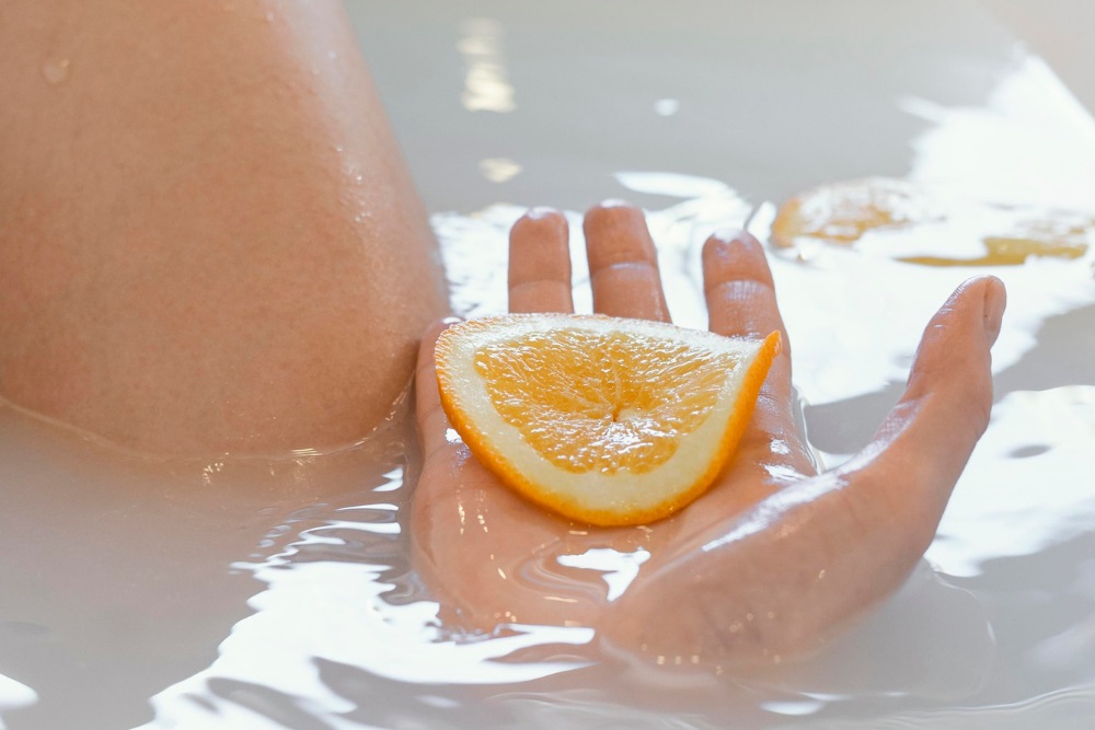 Žena koupající se ve vaně v citronové koupeli a držící na dlani plátek citronu