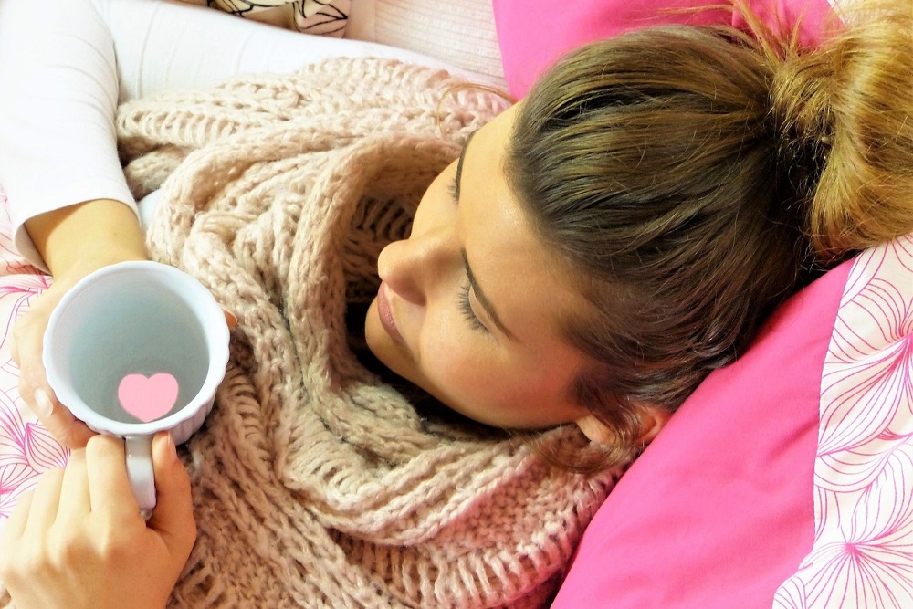 Mladá žena s hrnkem v posteli pije speciální čaj z oregana, cibule a jablka.