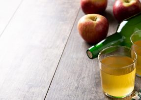 Sklenice s jablečným octem, zelenou lahví a jablky v pozadí