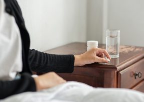 Žena natahující se pro prášek a sklenici vody stojící na nočním stolku