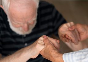 Ruce pomáhající za ruce starému pánovi s demencí