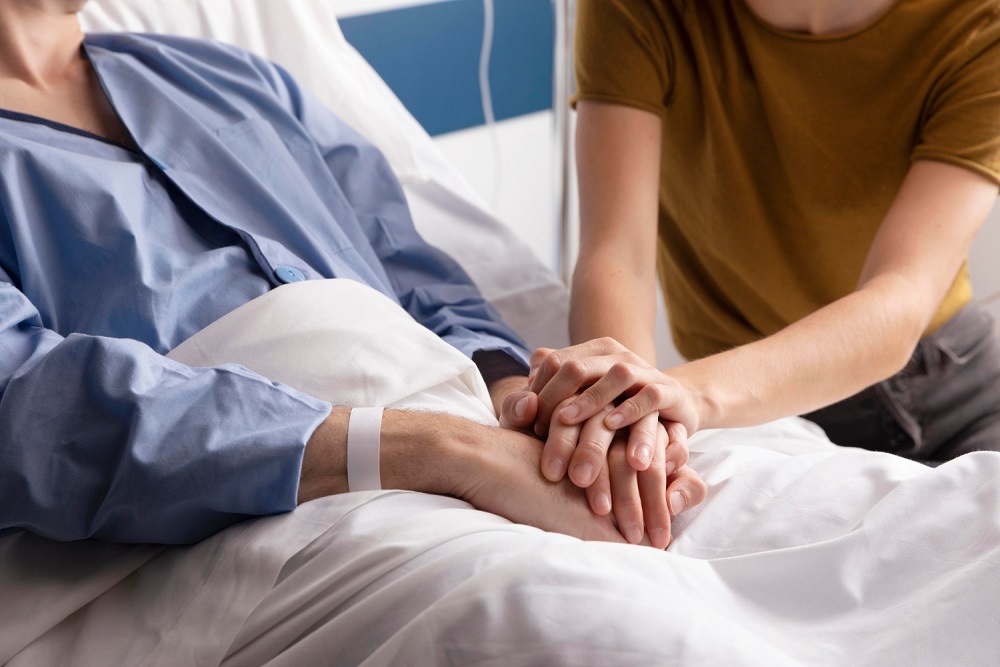 Žena držící za ruce muže na nemocničním lůžku