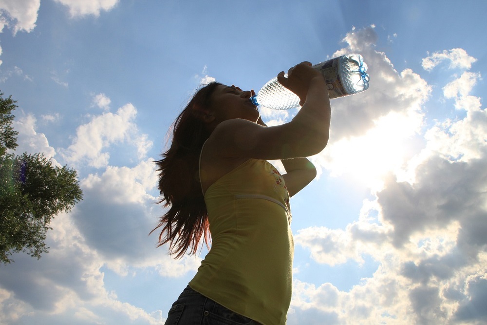 Žena focená proti slunci pijící vodu z lahve