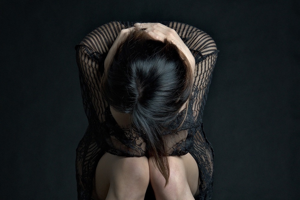 Černovlasá žena stočená v sedě do klubíčka prožívající smutek, zármutek a depresi
