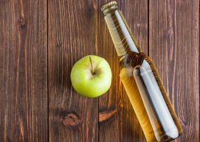 Jablečný ocet v láhvi s jablkem na dřevěném pozadí
