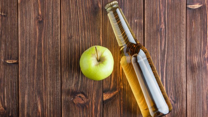 Jablečný ocet v láhvi s jablkem na dřevěném pozadí