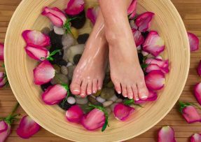 Nohy v lavóru s vodou a růžovými listy