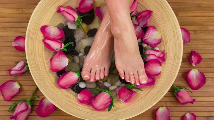 Nohy v lavóru s vodou a růžovými listy