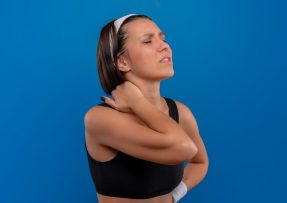 Žena ve sportovním sahající si za krk s tváří pokřivenou bolestí