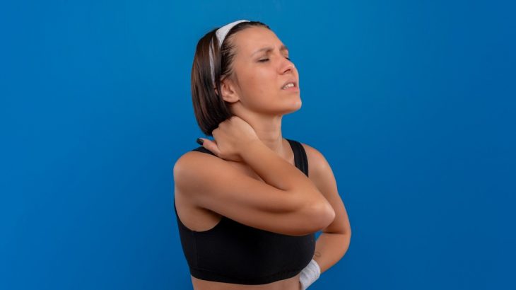 Žena ve sportovním sahající si za krk s tváří pokřivenou bolestí