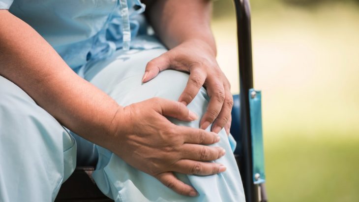 Pacient na vozíku držící se za bolavé koleno