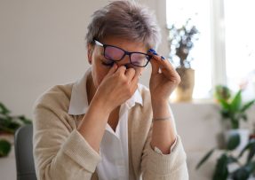 Starší žena držící si kořen nosu pod brýlemi