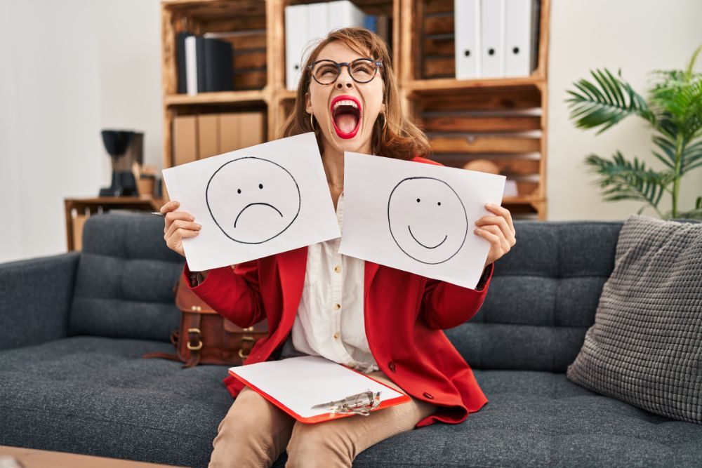 změny nálad, žena drží dva papíry - na jednom je nakreslený veselý smajlík, na druhé smutný
