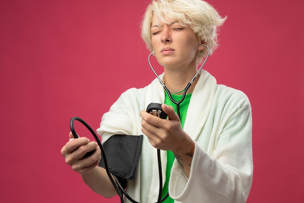 Žena měřící si tlak stetoskopem a manžetou