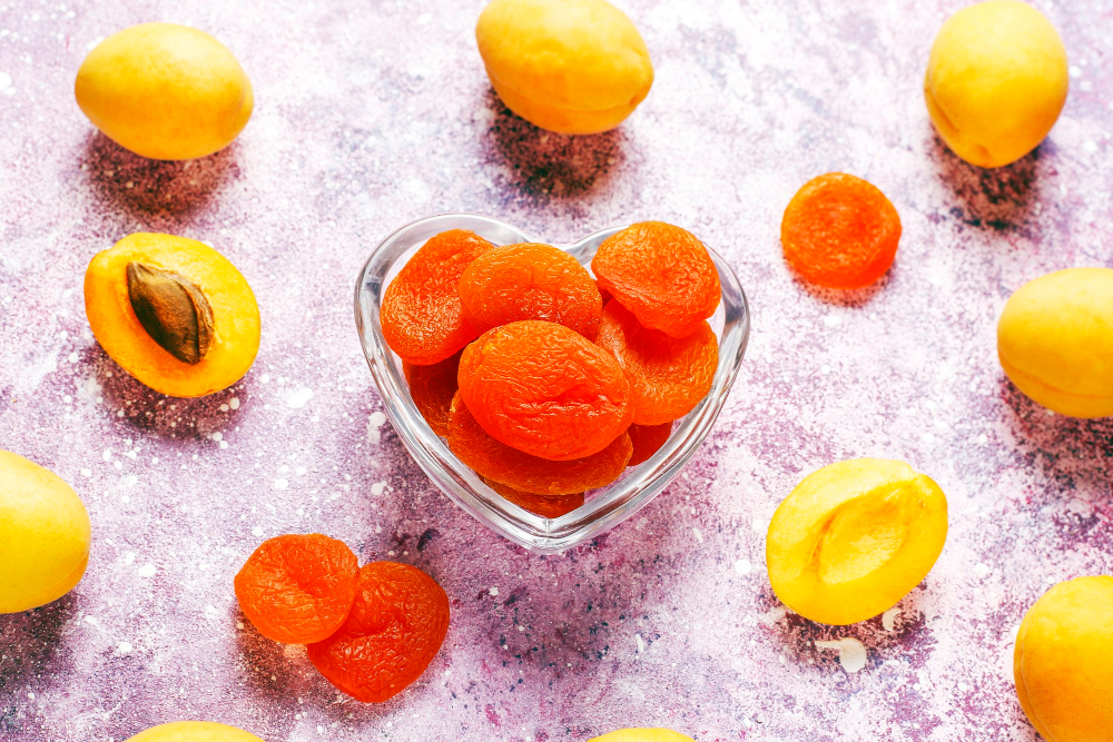 Sušené meruňky v misce tvaru srdce a čerstvé meruňky okolo