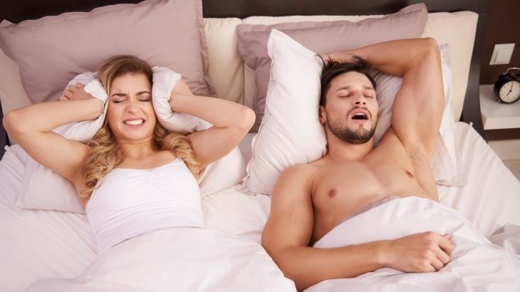 Muž chrápající v posteli a žena ucpávající si polštářem uši