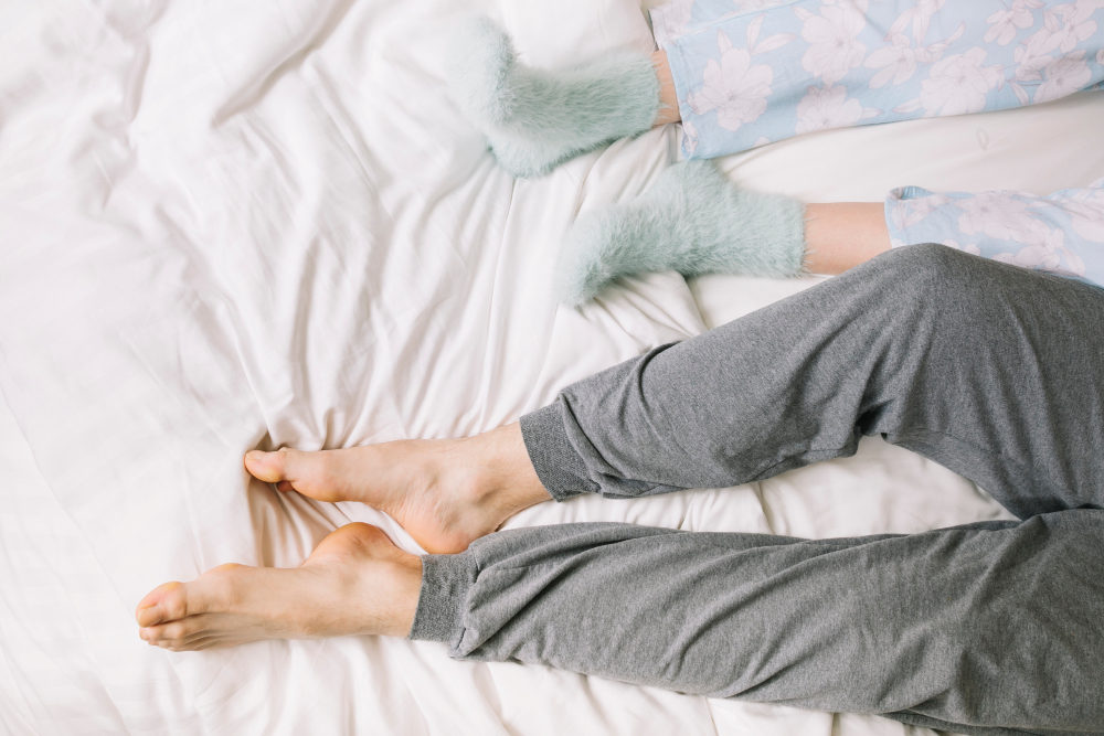 Pár v posteli – jedny nohy mají ponožky, druhé jsou holé